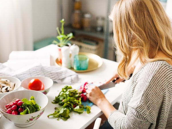 Mujer preparando una ensalada fresca en la cocina, rodeada de ingredientes.