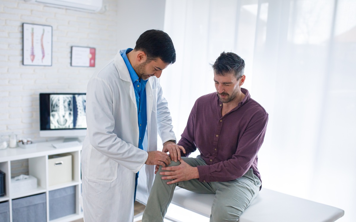 Médico traumatólogo evaluando la pierna de un paciente en consulta